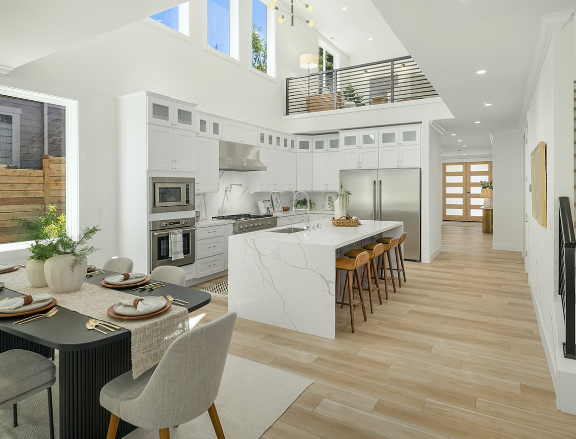 An open-concept living area with a high ceiling, large windows, and a marble countertop kitchen island, demonstrating a spacious and bright interior design.