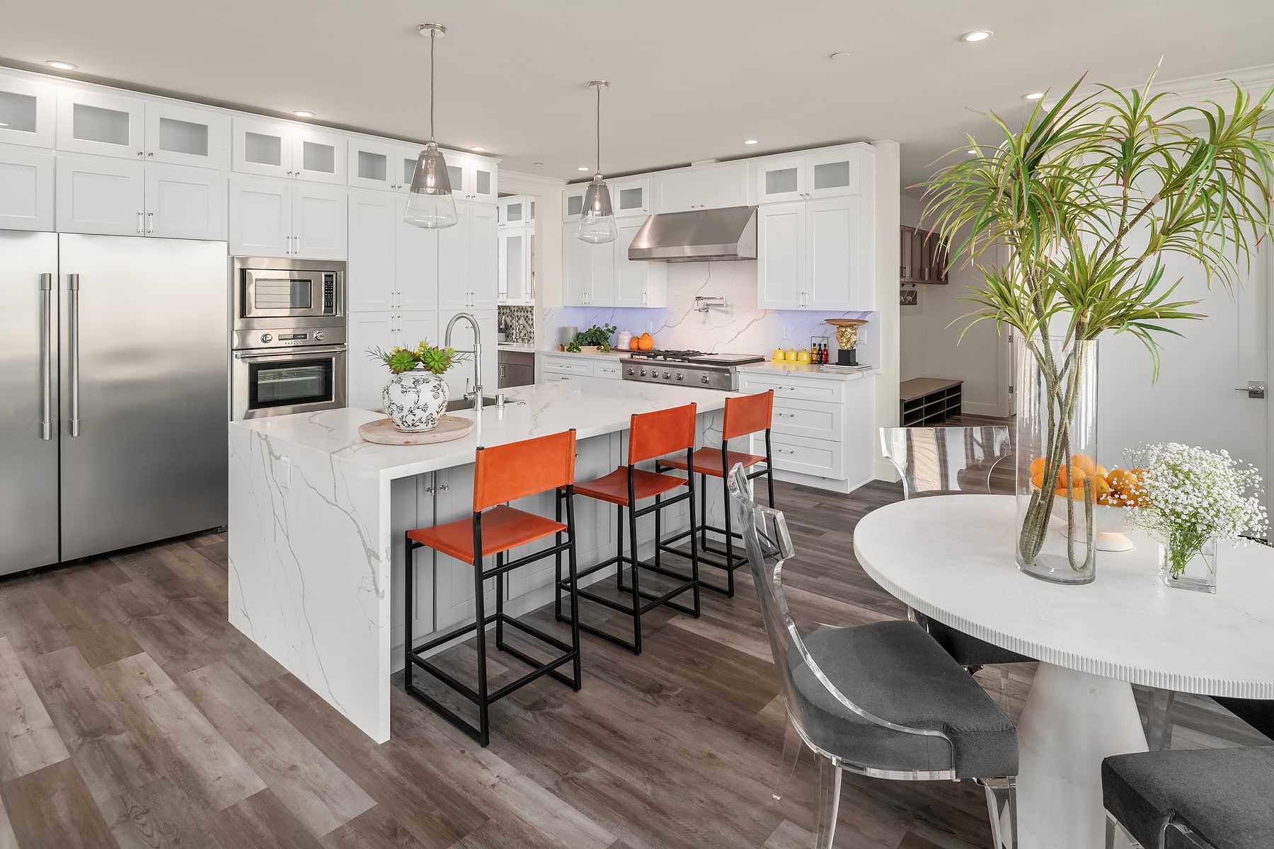 A modern kitchen with white cabinets, a large island with a waterfall countertop, and stainless steel appliances, showcasing a clean and elegant design.