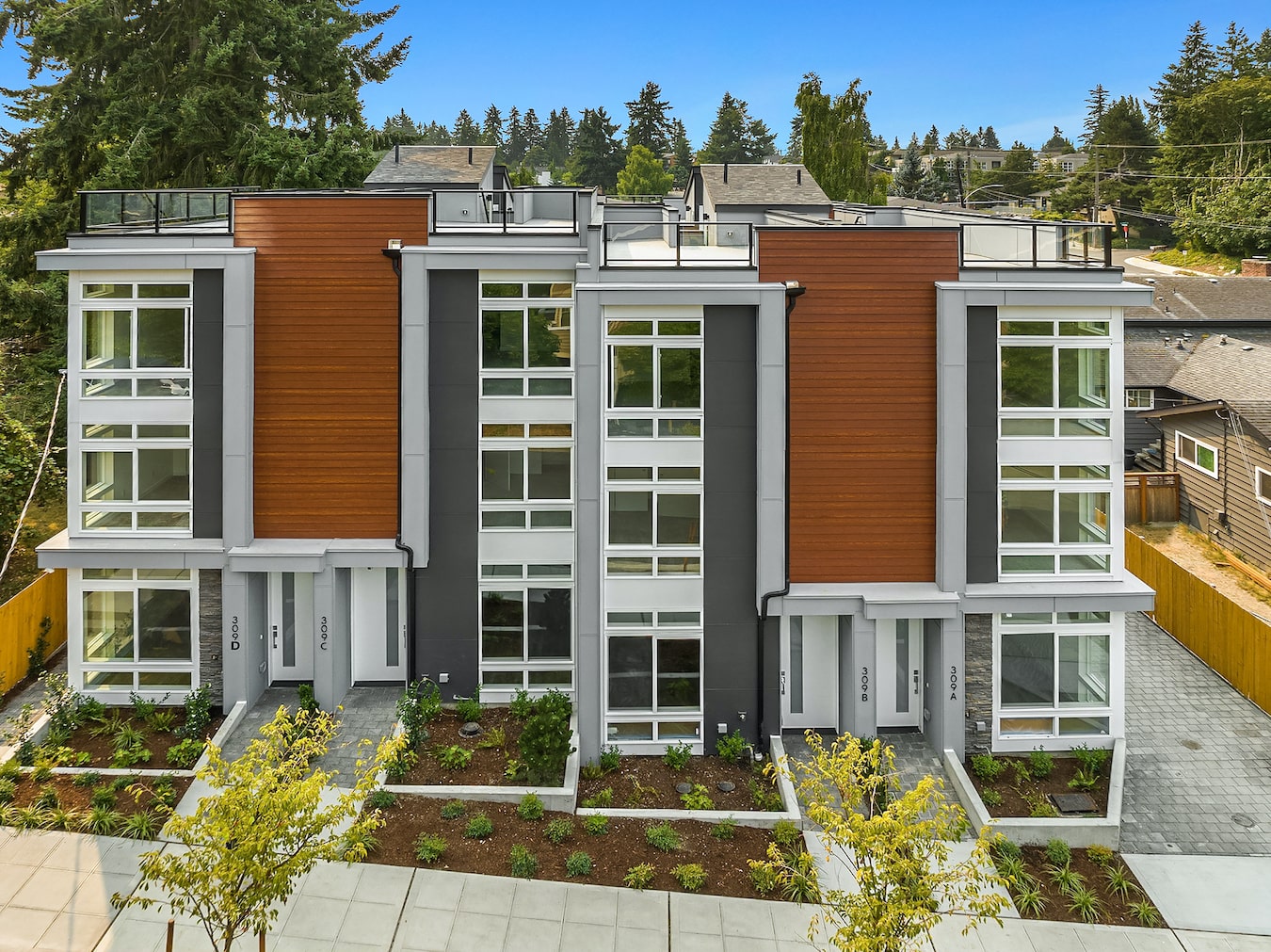 An exterior view of a block of modern, multi-story townhomes with wood and gray siding, showcasing the urban architectural style by TP Home Builds.