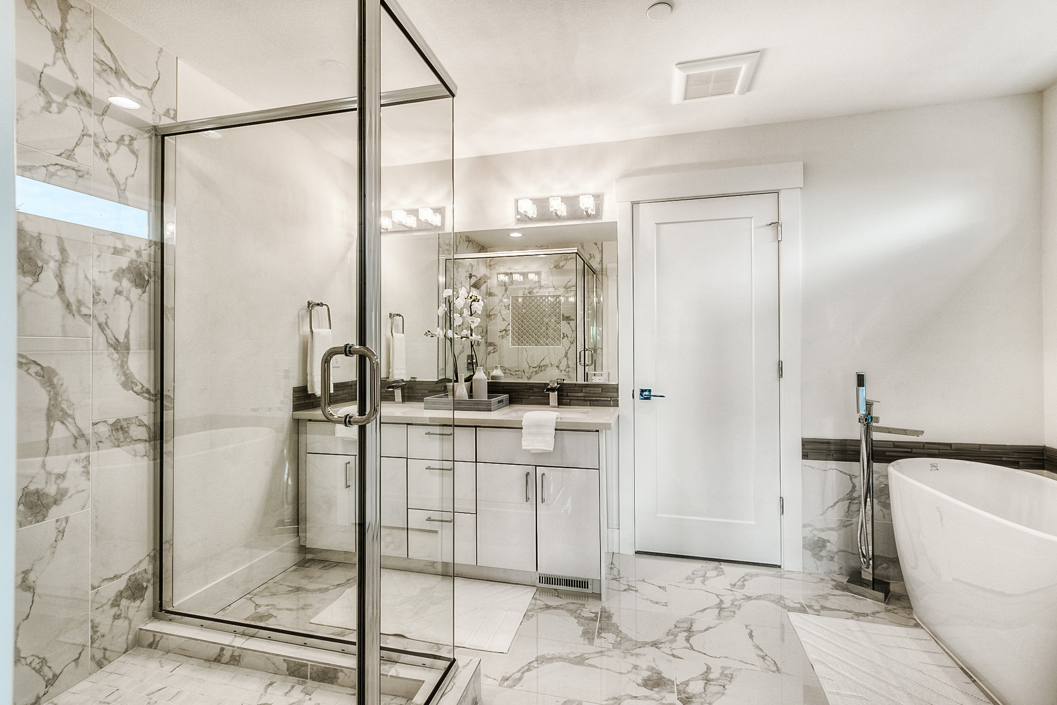 A lavish bathroom with striking marble-patterned tile, a large glass shower, and a clean white vanity, featuring high-quality surfaces from Oscar Surfaces.