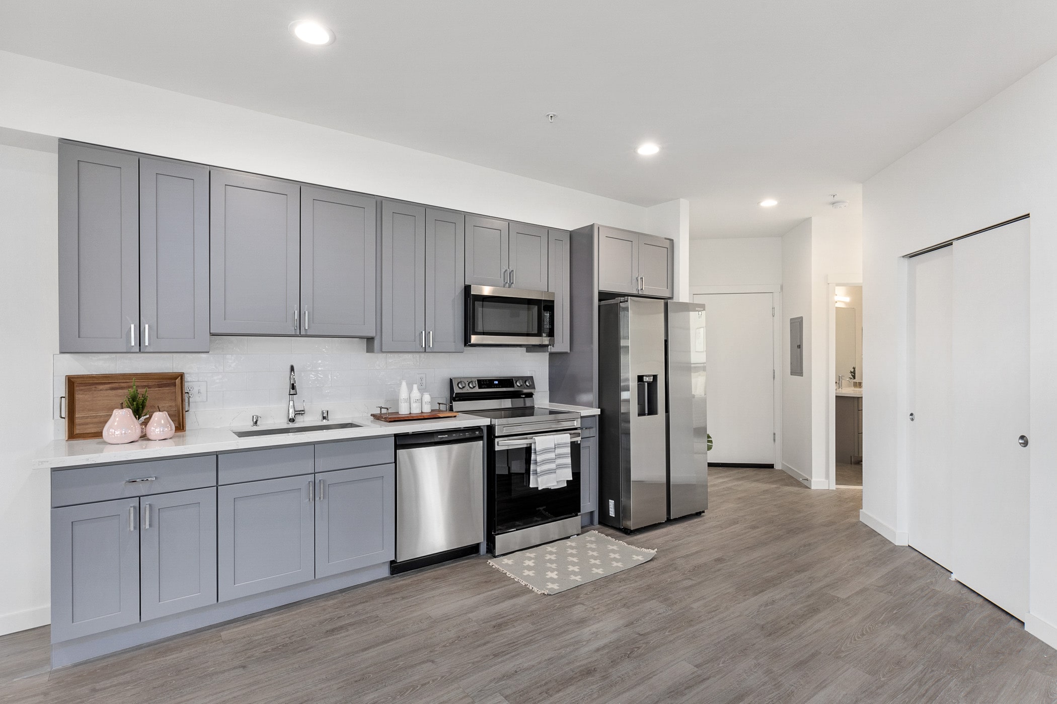 A modern apartment kitchen with sleek gray cabinets, white countertops, and stainless steel appliances, showcasing an interior from the Shoreline apartments by TP Home.
