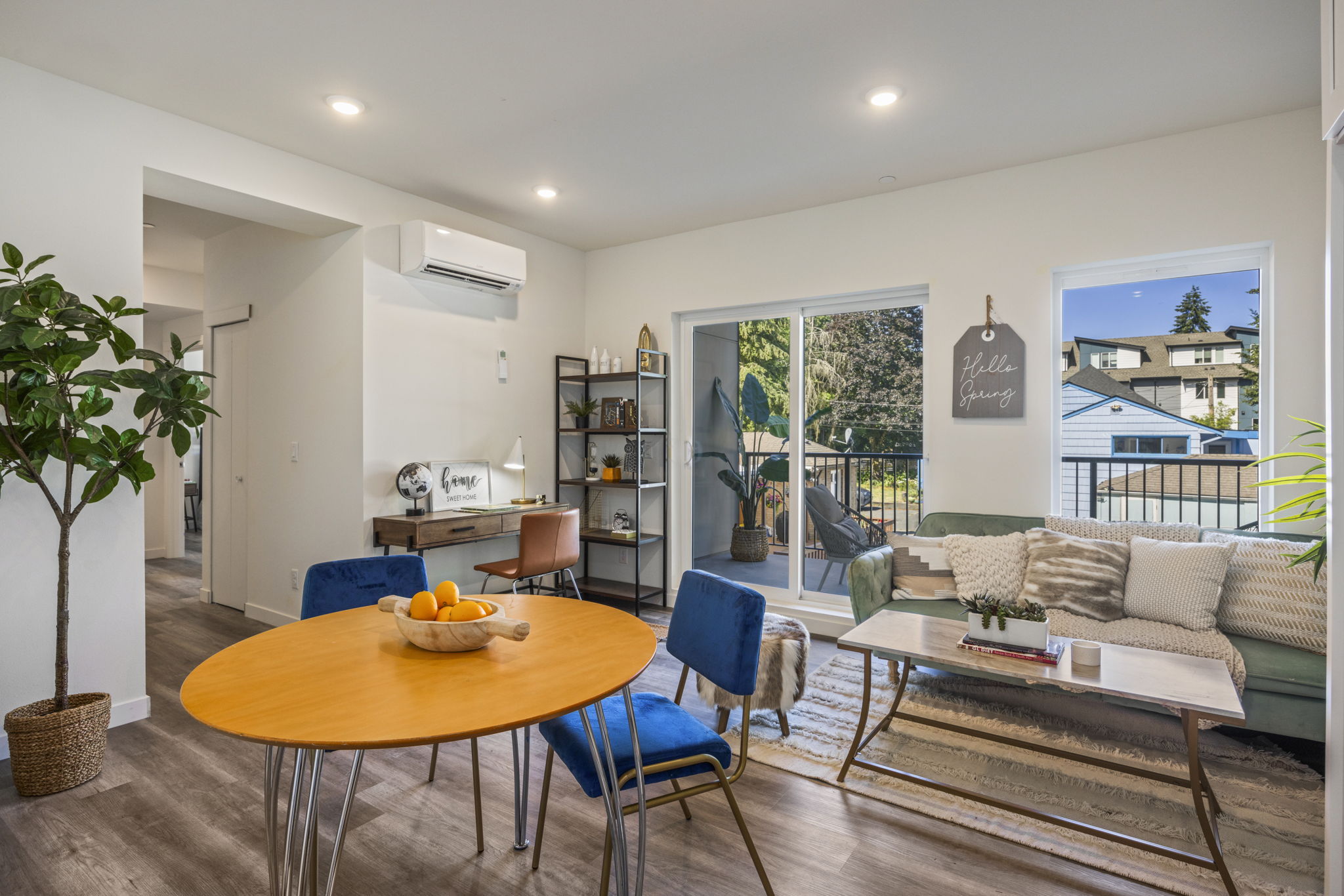 A modern open-concept living space with a dining area, featuring a couch with throw pillows and a desk nook, highlighting the flow and design.
