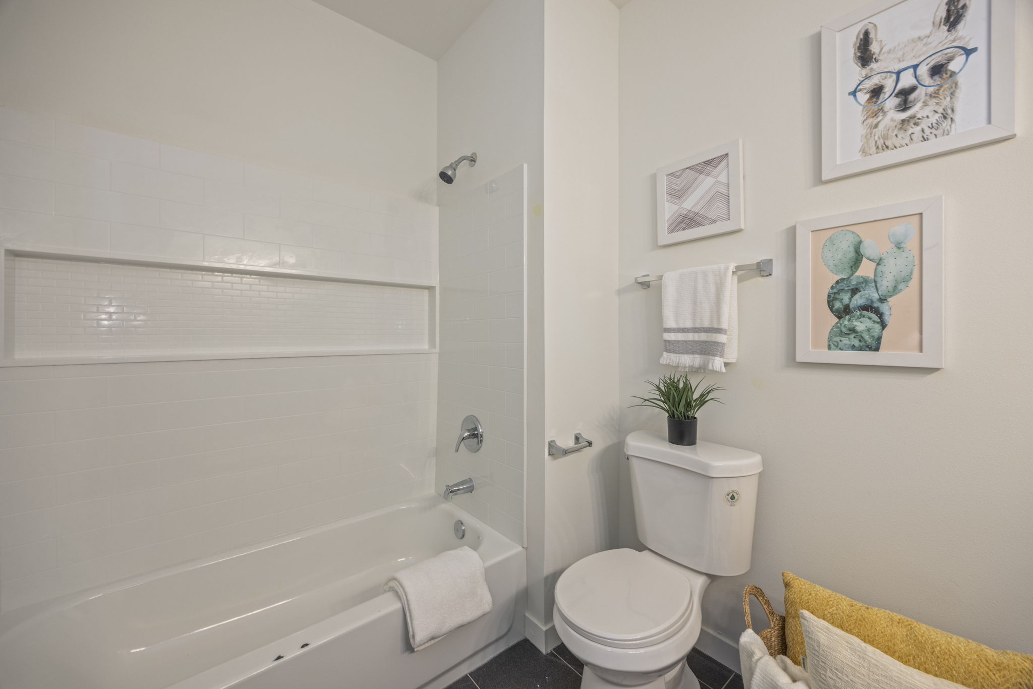 A modern bathroom featuring a white subway tile bathtub, a toilet, and playful wall art, demonstrating a clean and minimalist interior design.