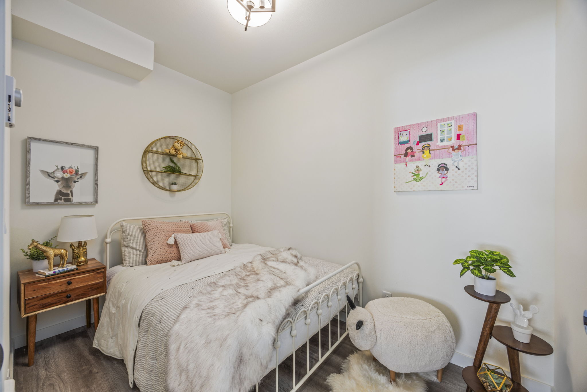 A small bedroom with a metal-framed bed, wood furniture, and whimsical wall decor, showcasing a compact and charming room design.