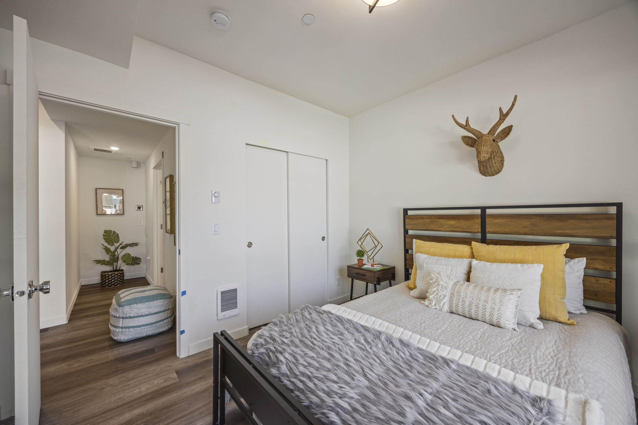 A modern bedroom with a wood-panel headboard, yellow and gray pillows, and a deer bust on the wall, highlighting a cozy and unique interior.