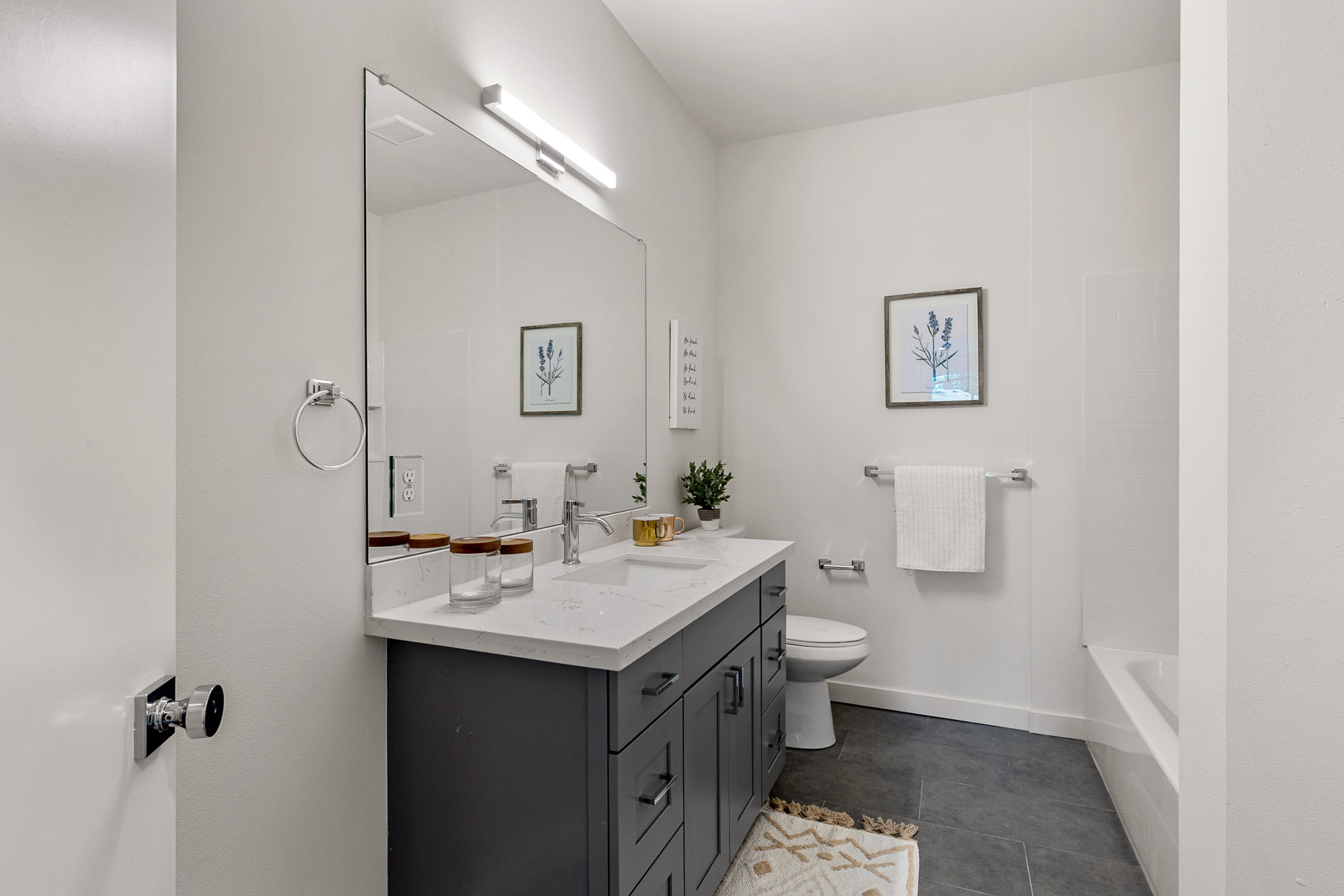 A modern bathroom in a Shoreline apartment, featuring a dark gray vanity, a large mirror, and high-quality surfaces provided by Oscar Surfaces.