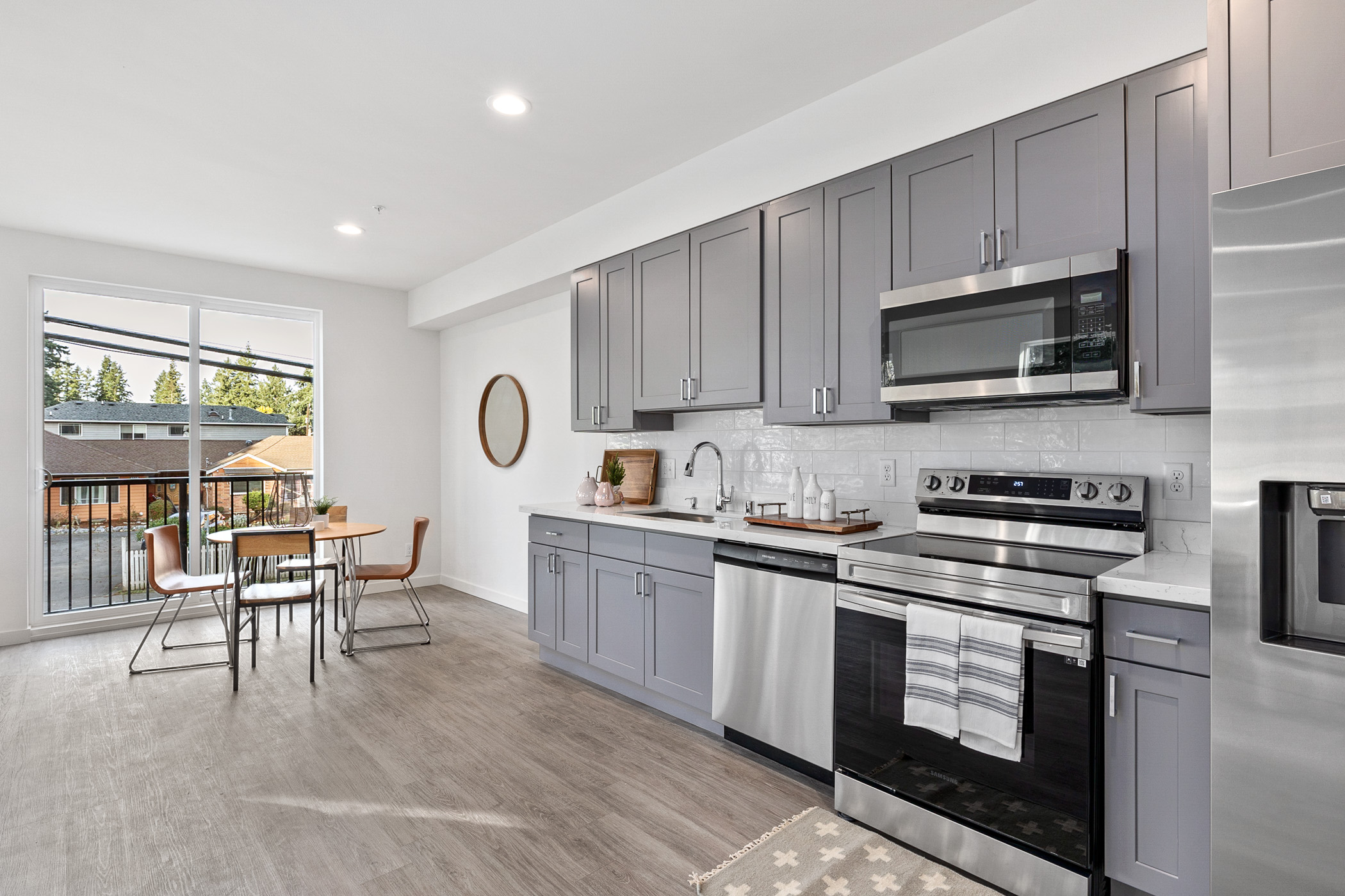 An apartment kitchen with gray cabinets, a white countertop, and a small dining area, highlighting the compact yet functional design of TP Home's Shoreline project.