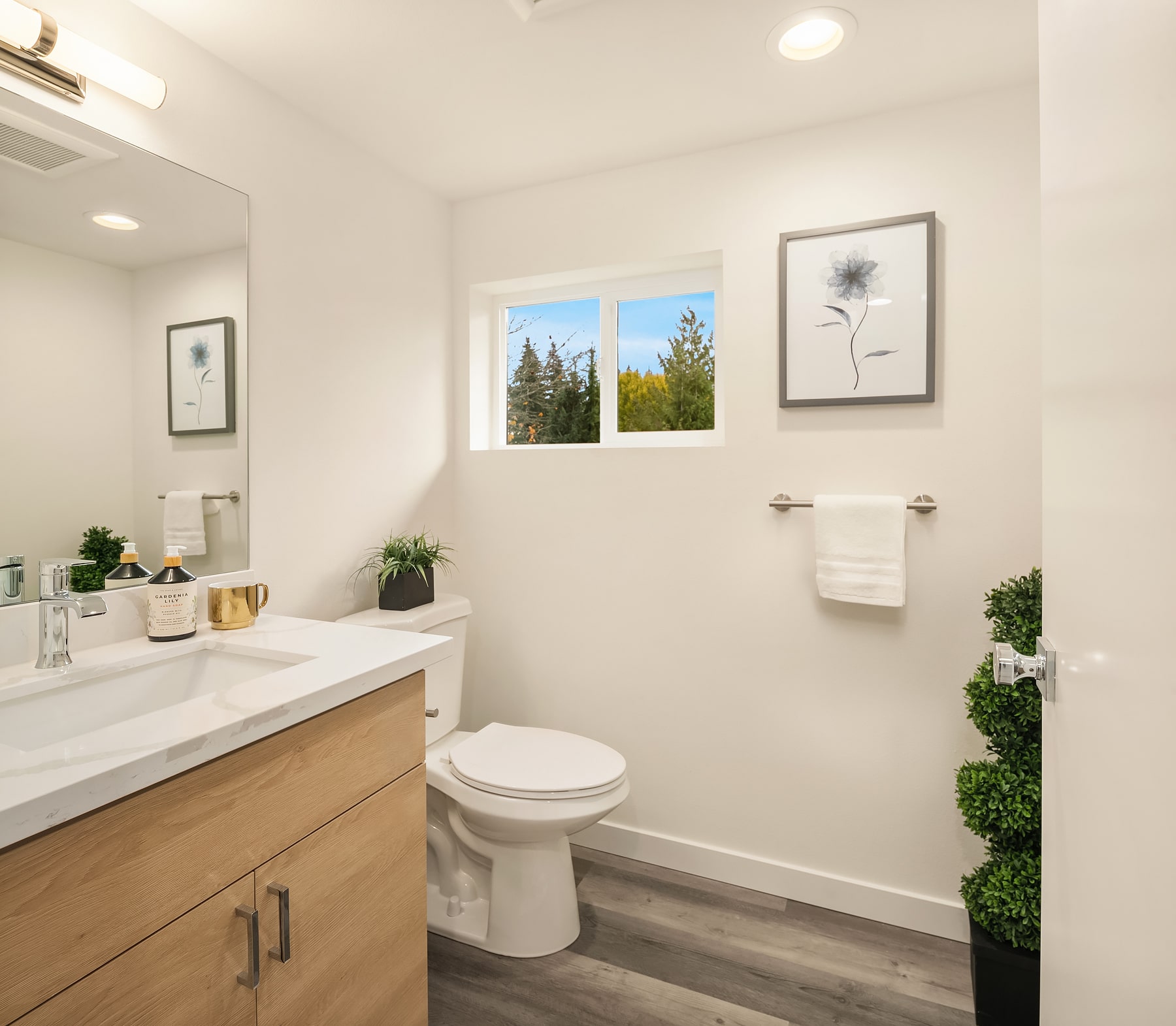 A well-lit apartment bathroom with a light wood-tone vanity and white countertop, representing a standard, clean interior finish in the Shoreline apartments.