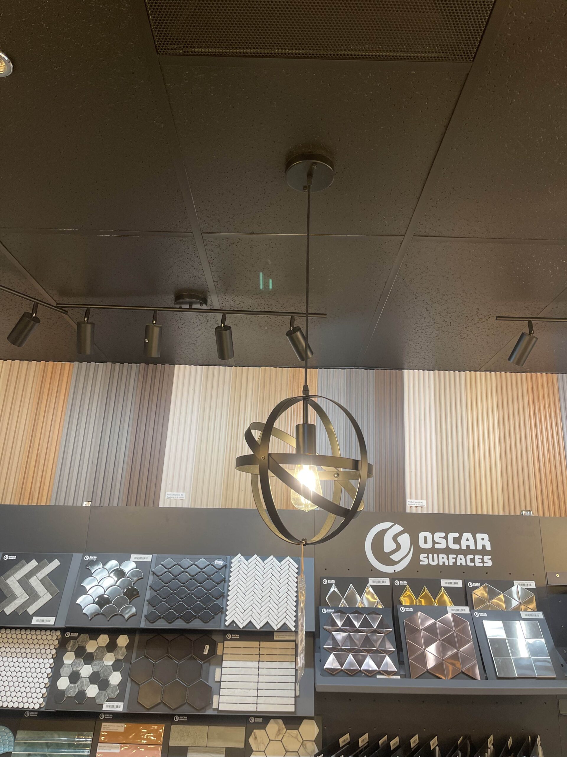 A stylish, modern light fixture on display against a wall of geometric and mosaic tiles, representing the lighting options at the Oscar Surfaces showroom.