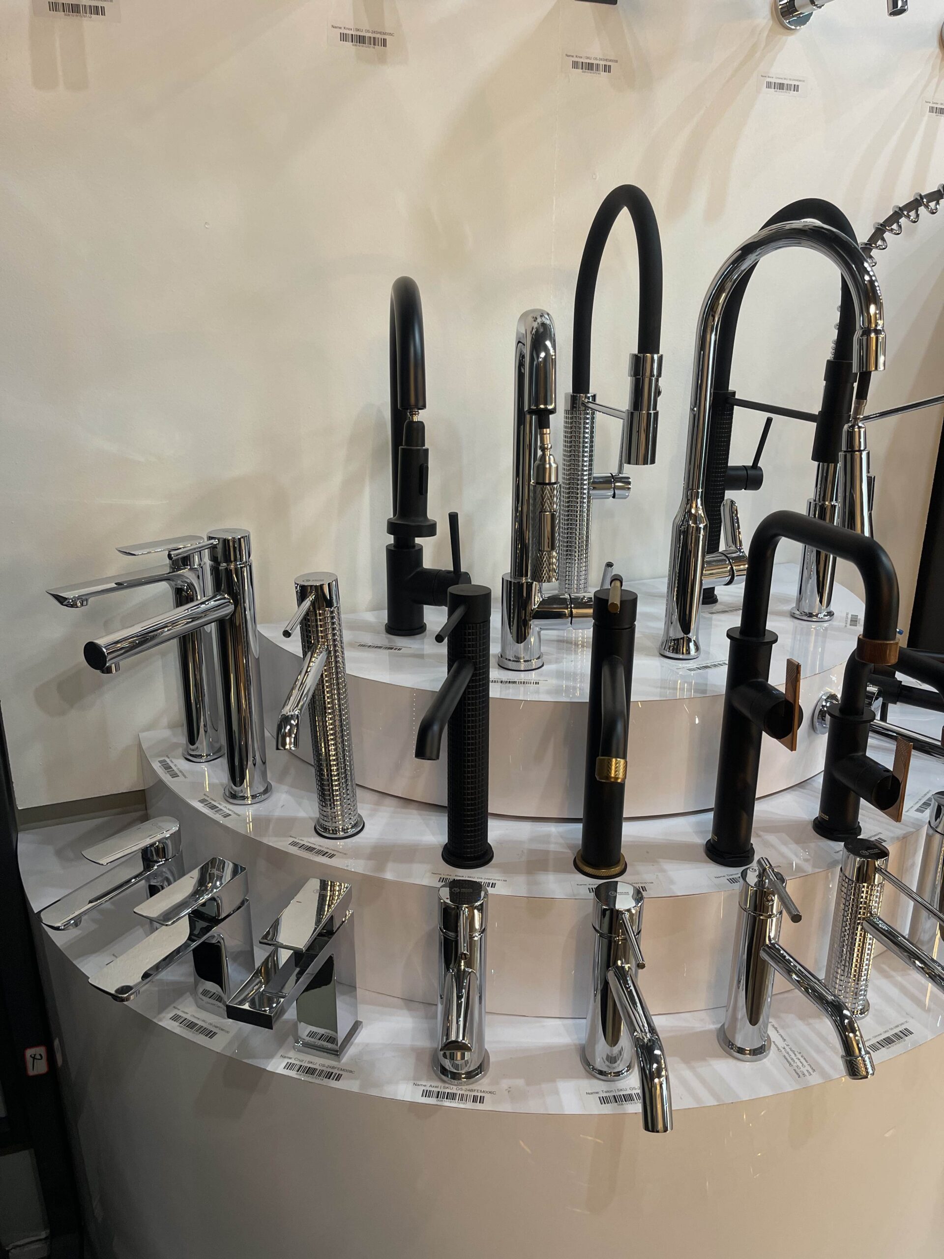 A display of various modern kitchen and bathroom faucets in black, chrome, and brushed metal finishes, showcasing hardware options available at the showroom.