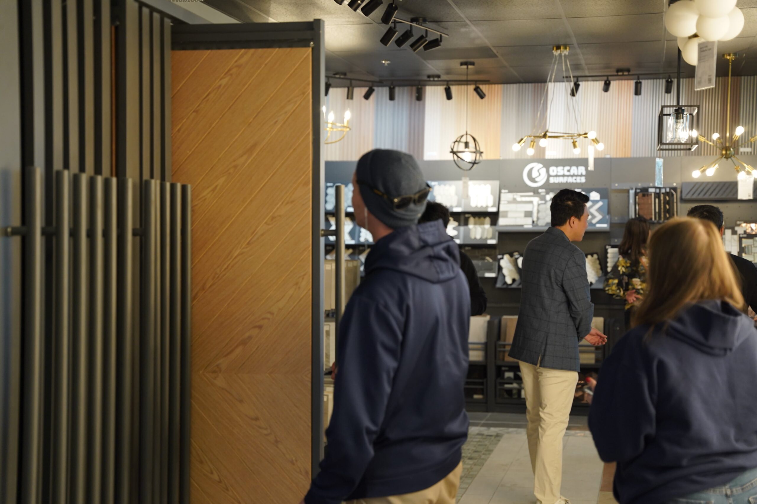 Customers browsing the interior of the Oscar Surfaces showroom, with displays of wood-look panels, lighting fixtures, and surfaces, showcasing a modern retail environment.