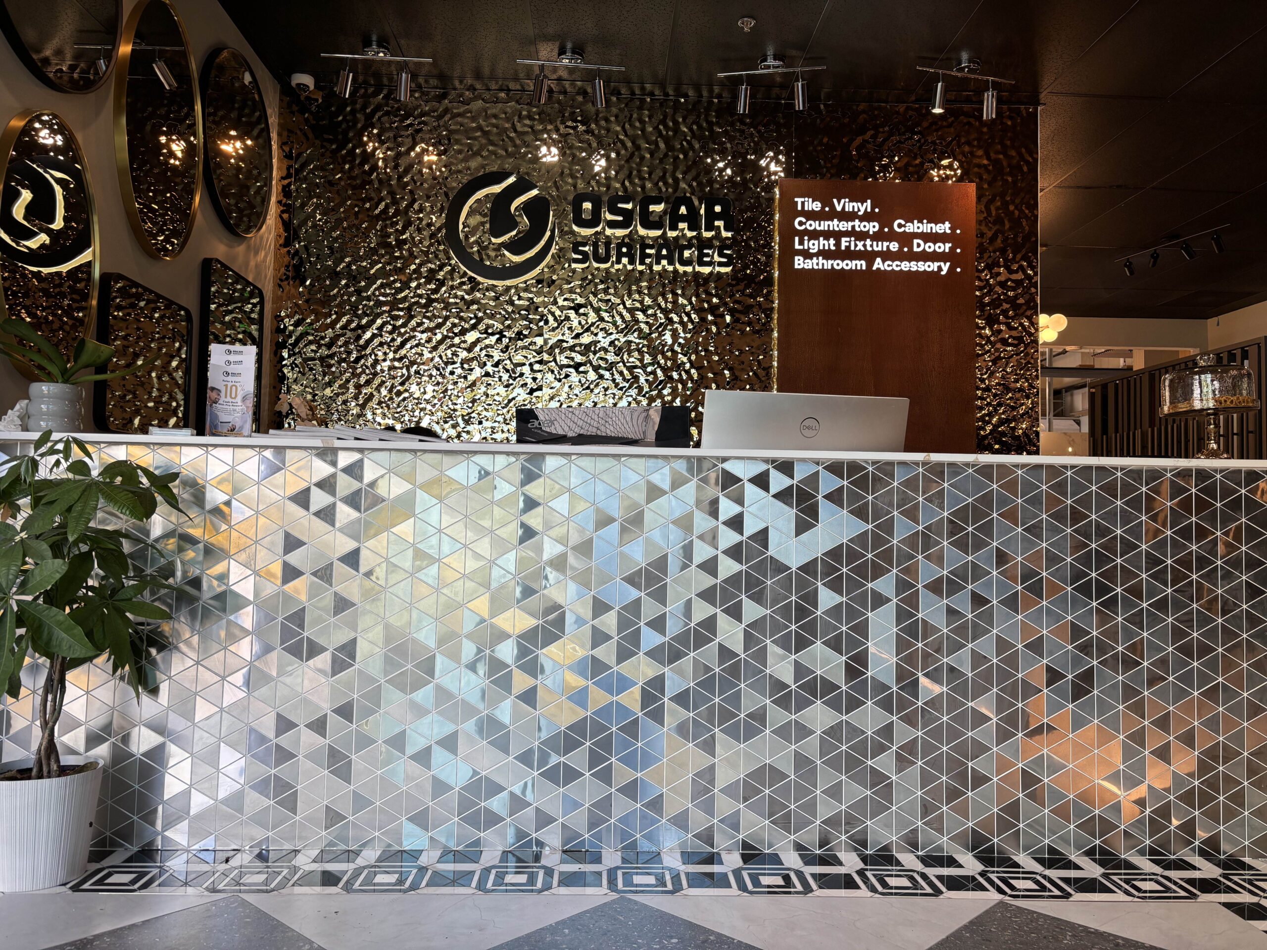 The reception desk of the Oscar Surfaces showroom, featuring a striking mosaic tile counter and textured wall, highlighting the quality of finishes available.