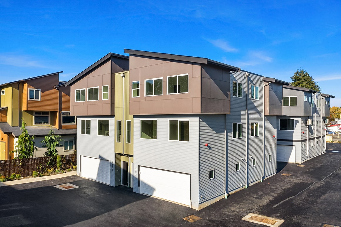An aerial view of a block of modern townhomes with contrasting gray and brown siding, showcasing the completed architecture of an ADHG development.