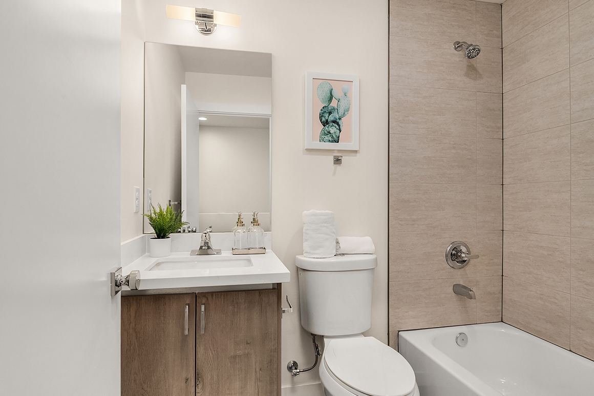 A modern bathroom with a light wood vanity, white countertop, and beige tiled shower, representing a clean and contemporary interior finish.