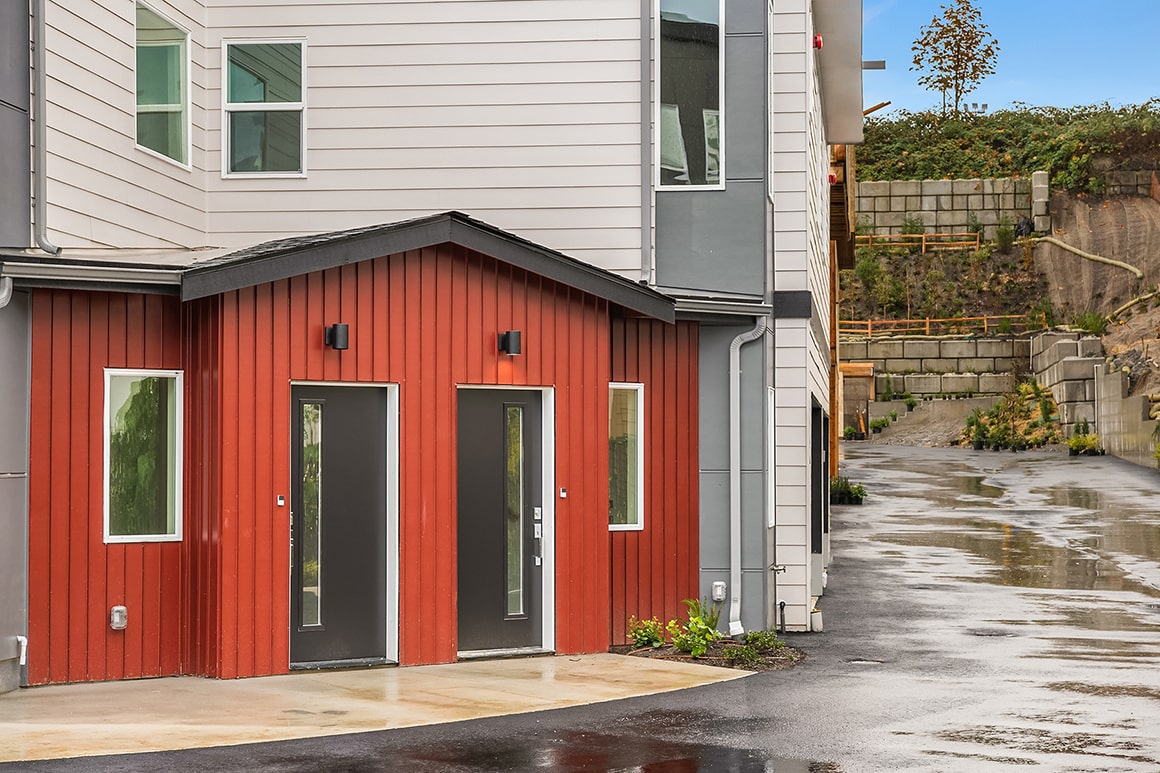 A modern home entrance with a striking red exterior and a covered entryway, showcasing a bold design choice in an exclusive ADHG development.