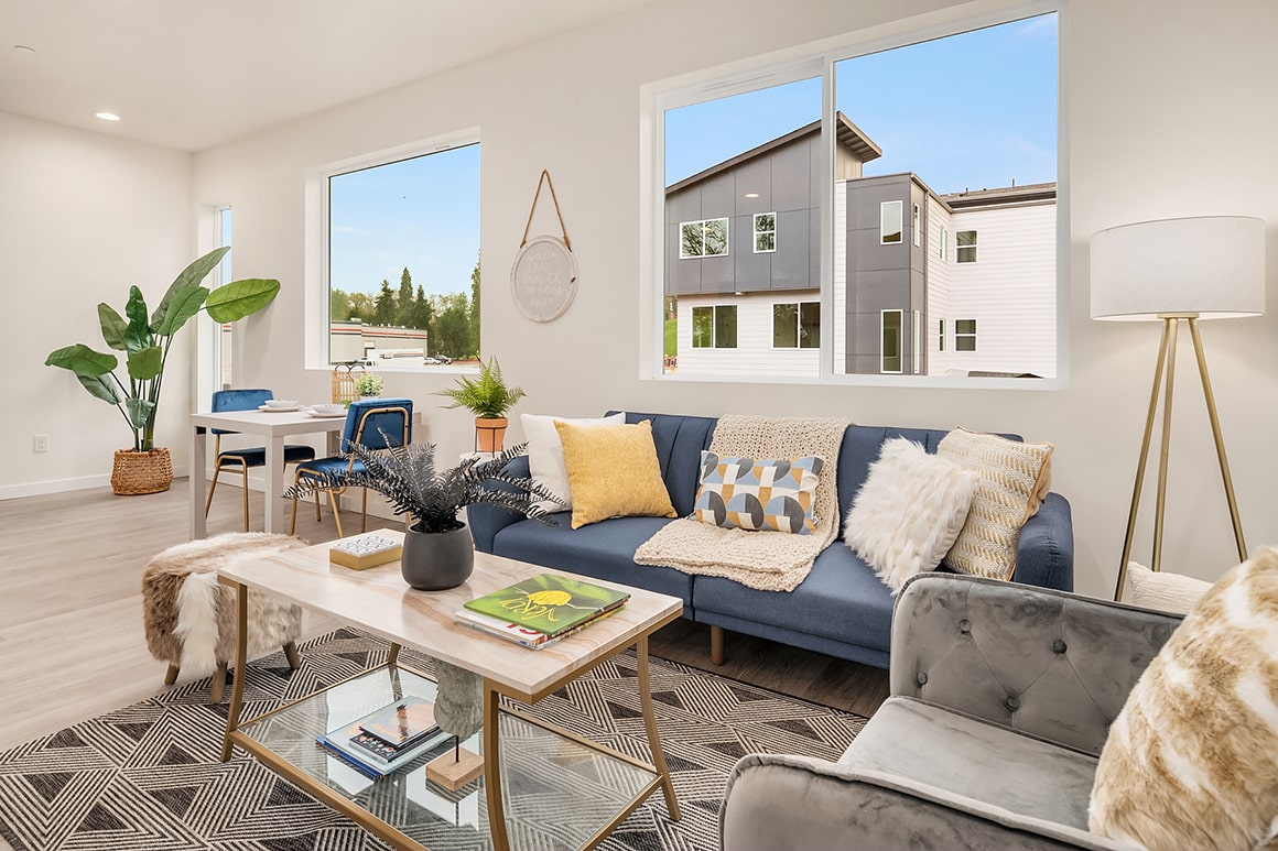 A bright and modern living room with a blue sofa, a glass coffee table, and large windows, highlighting the comfortable and stylish interiors.