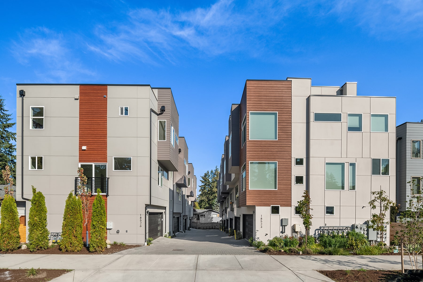 A row of newly built modern townhomes with wood and gray siding, showcasing the clean and contemporary exterior design of an ADHG development.