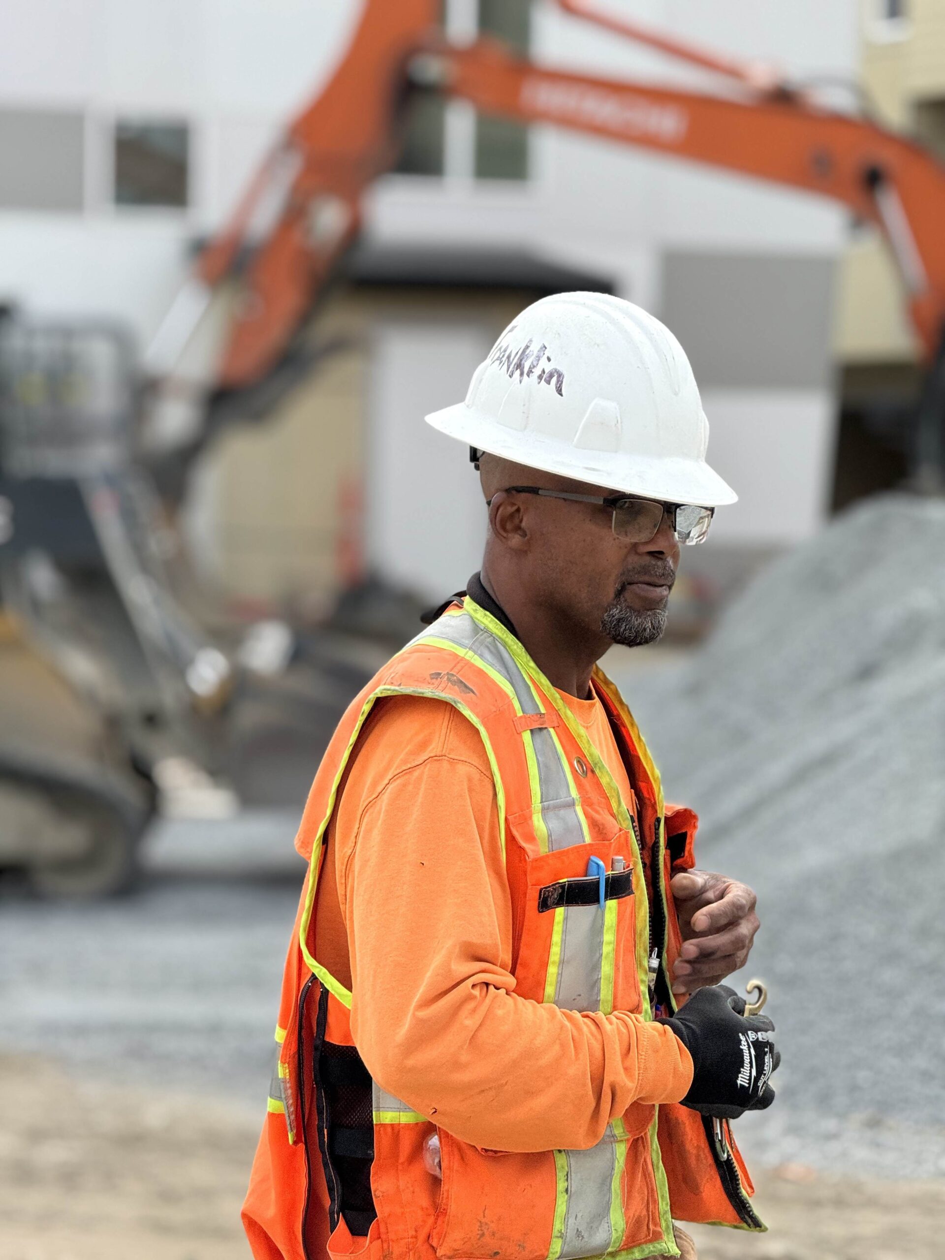 A construction worker in a hard hat and safety vest stands on a job site, representing the professionalism and dedication of the team building ADHG developments.