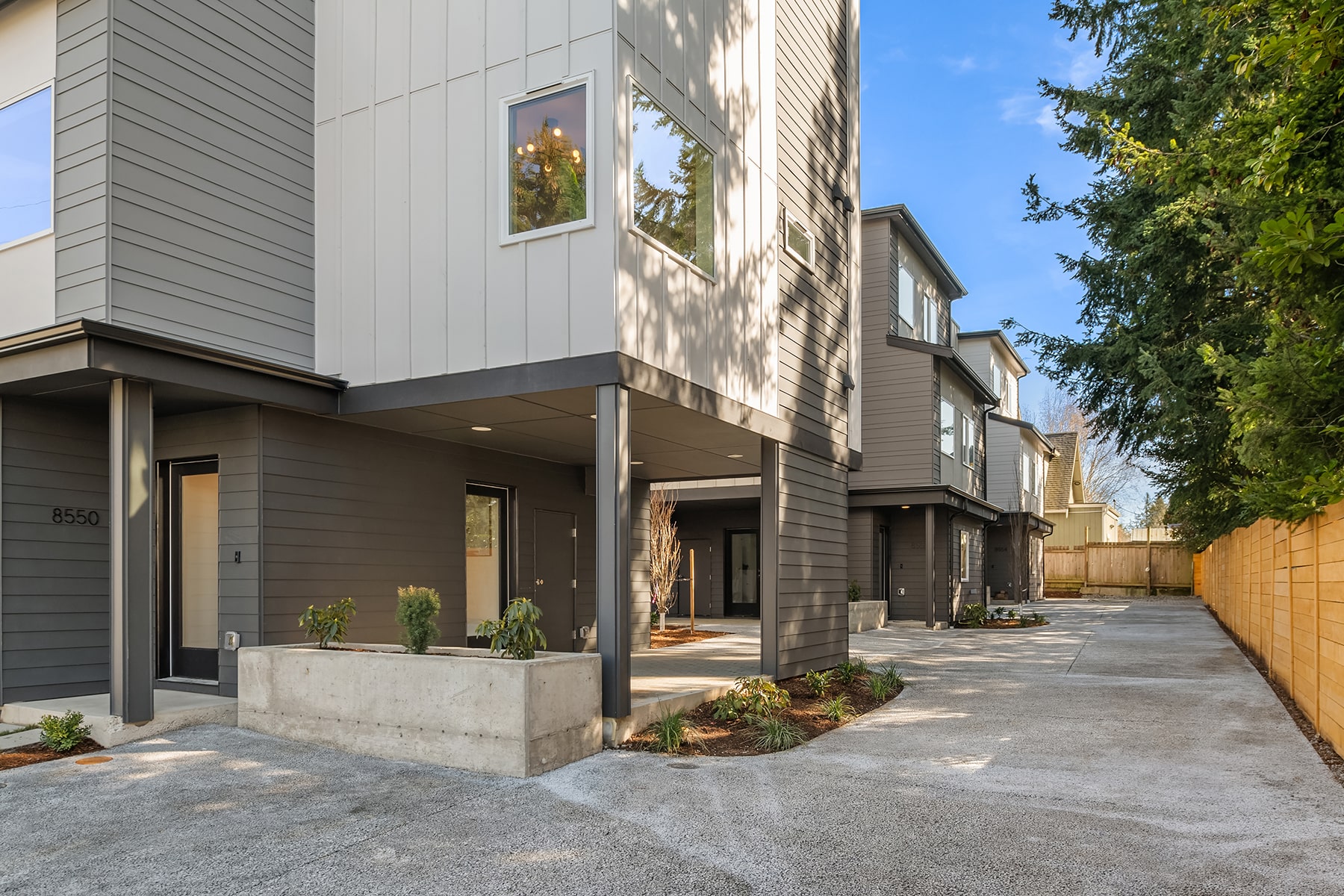 The covered entryway and parking area of a modern townhome, featuring a minimalist design with concrete pavers and vertical wood siding.