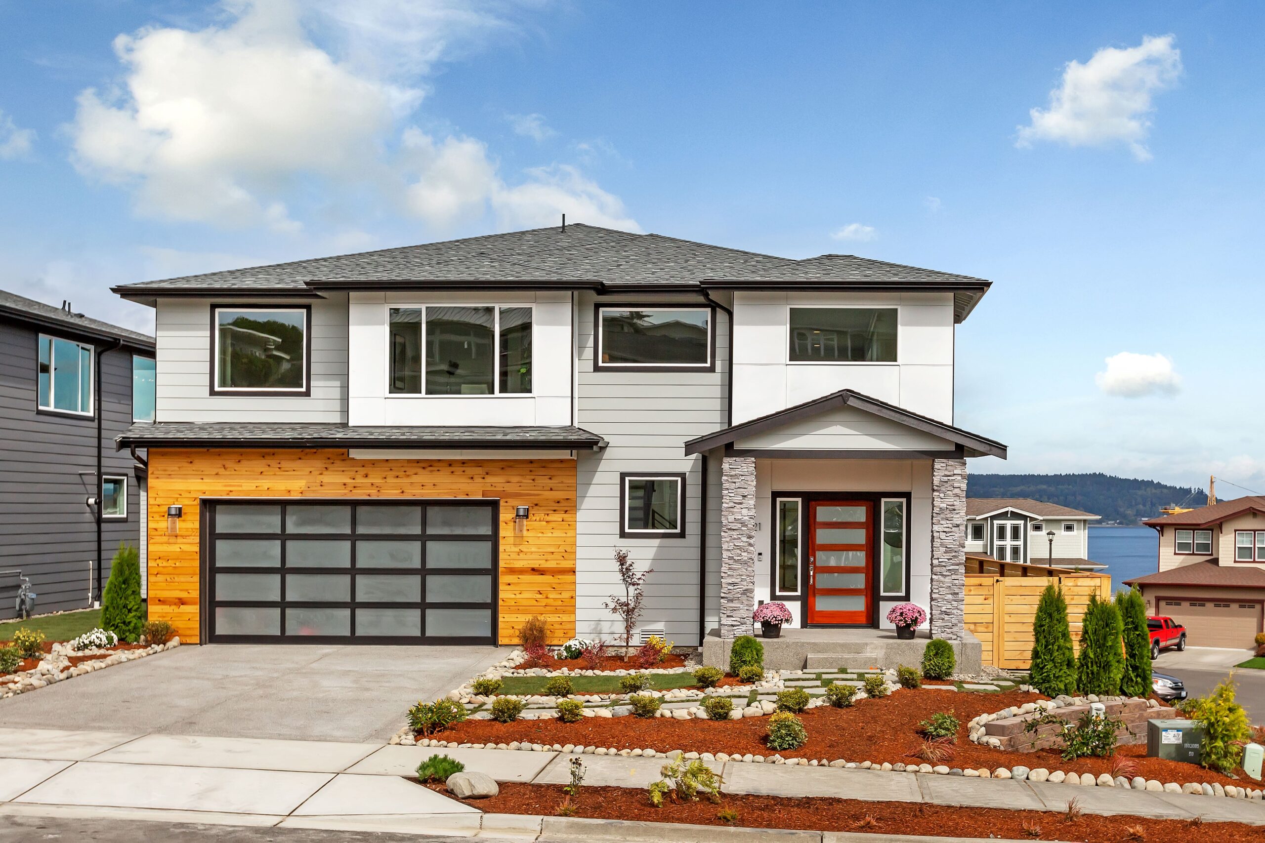The exterior of a newly built contemporary home with a clean gray and white facade and a wood-panel garage door, showcasing a luxury ADHG development.