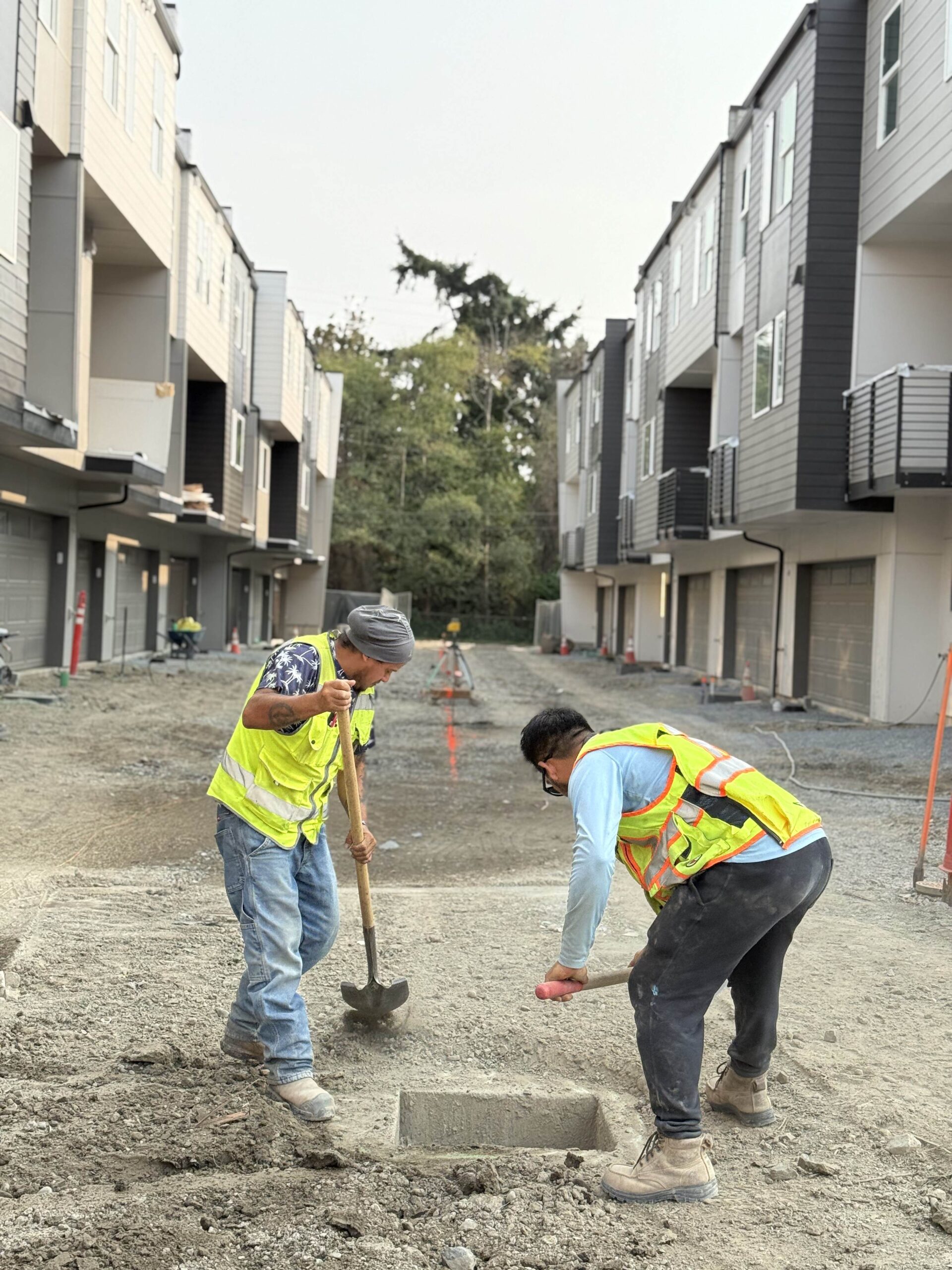 Two construction workers in safety vests use shovels on a building site, demonstrating the groundwork done by TP Home's excavation partners.