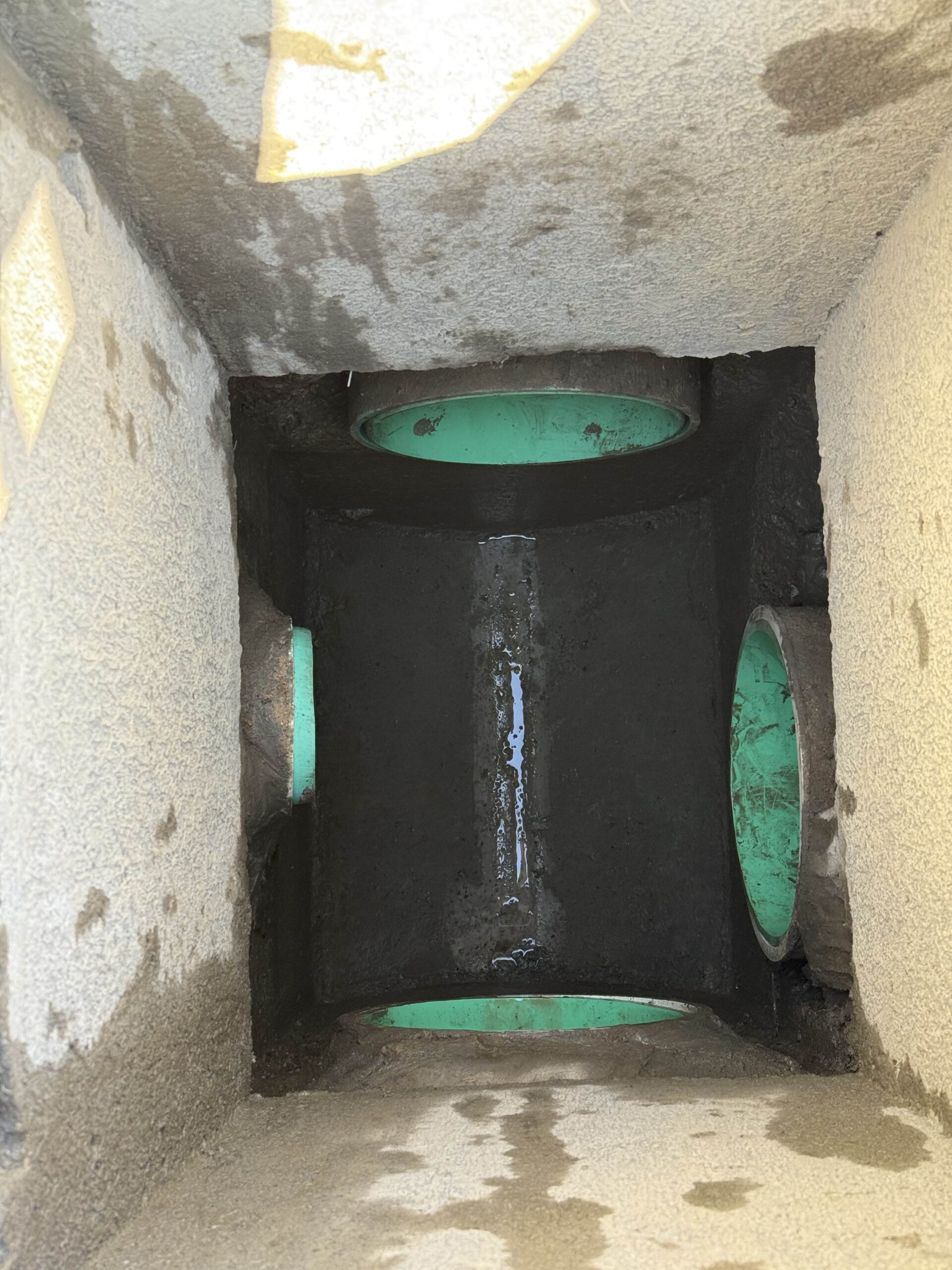 A view inside an excavated drainage structure with green pipes, highlighting the precision work for underground utilities in a construction project.