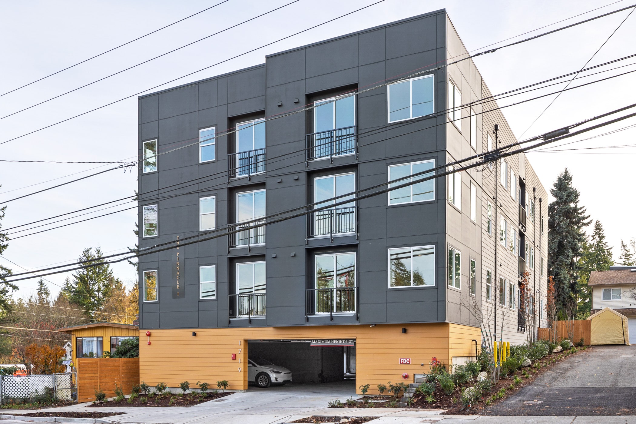 A newly completed multi-story apartment building with a dark gray exterior and a covered ground-level parking area, showcasing a finished commercial project.