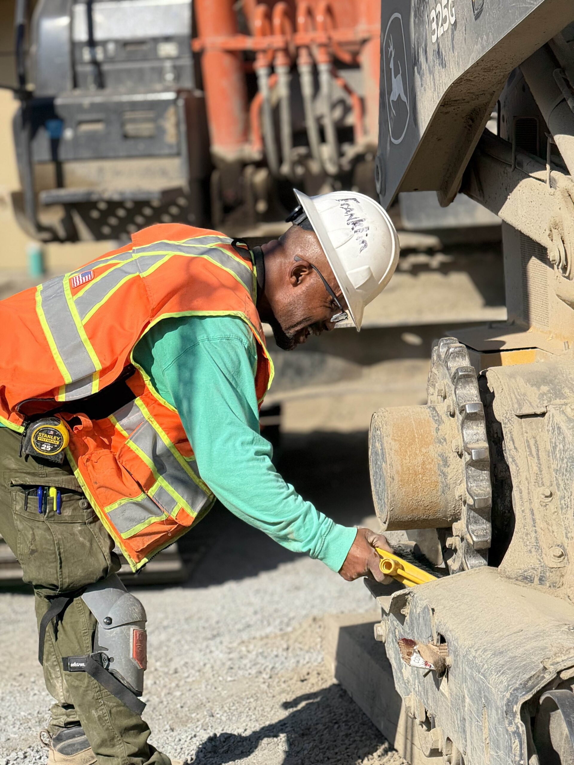 A construction worker inspects the tracks of a large excavator, highlighting the meticulous attention to detail and maintenance on-site.