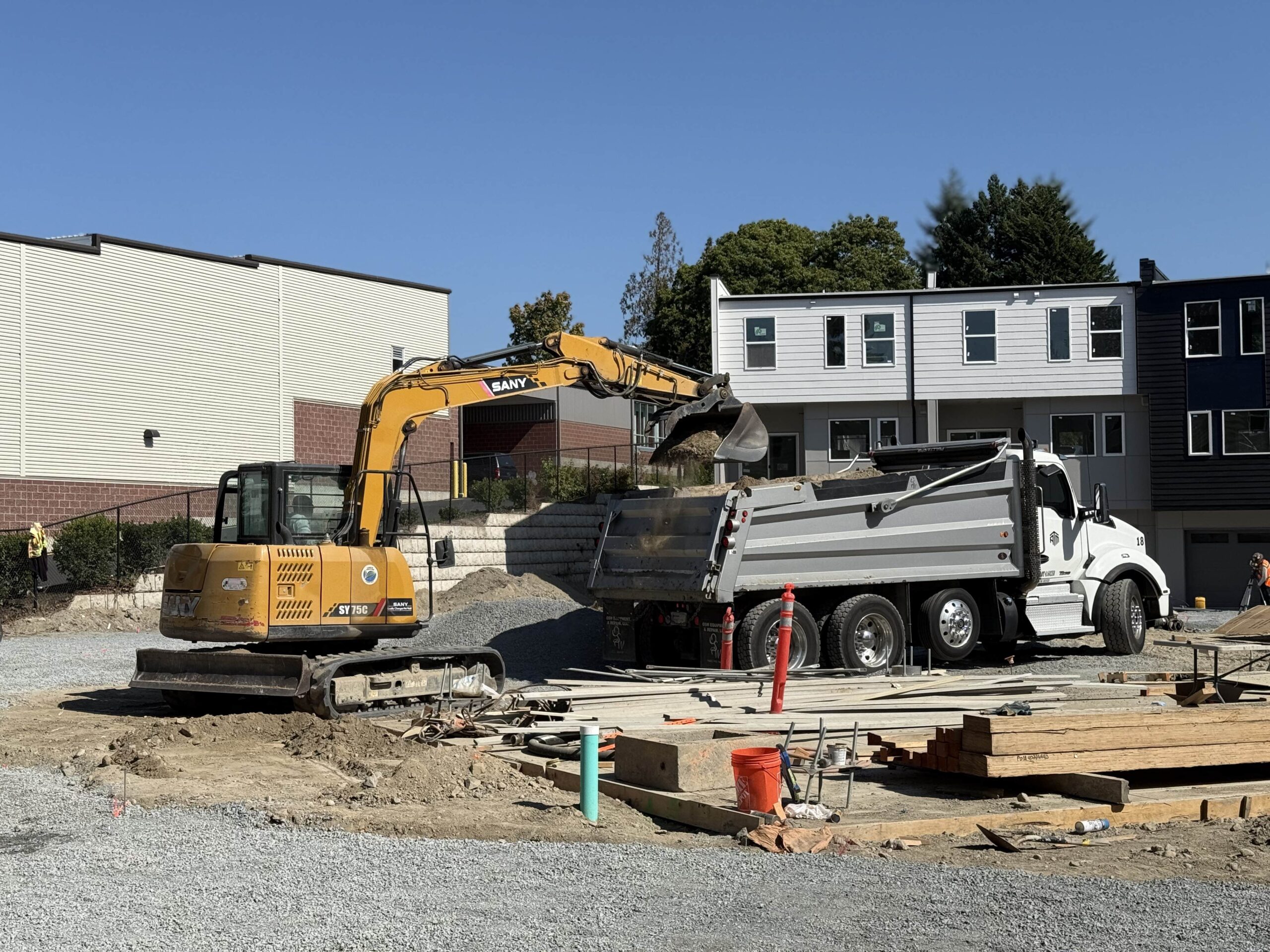 A Sany excavator loads a dump truck at a construction site, showcasing the heavy equipment used by TP Home's excavation partner for new builds.