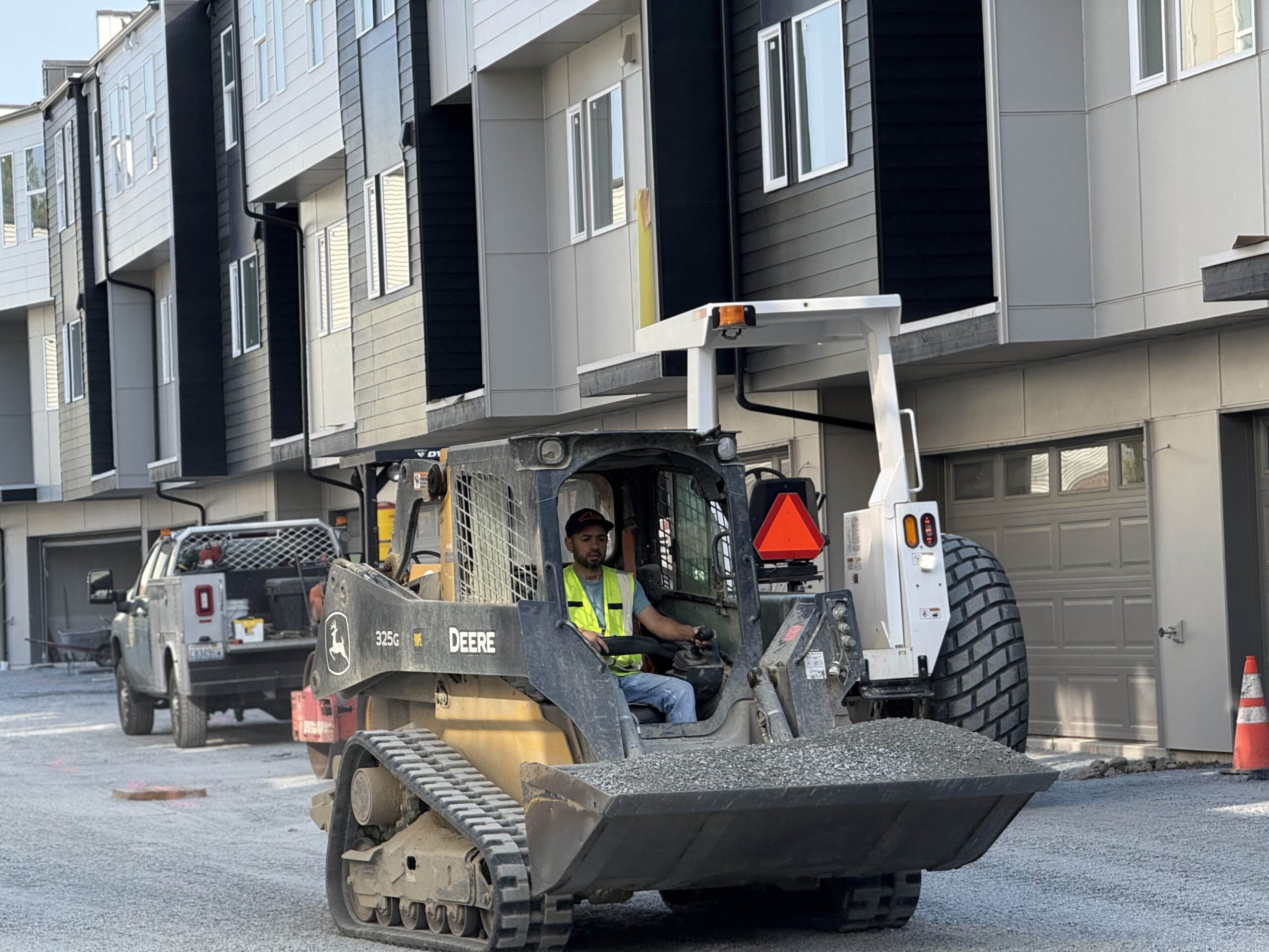 A worker operates a small Bobcat excavator, carrying gravel to a site, highlighting the efficient machinery used for construction projects.