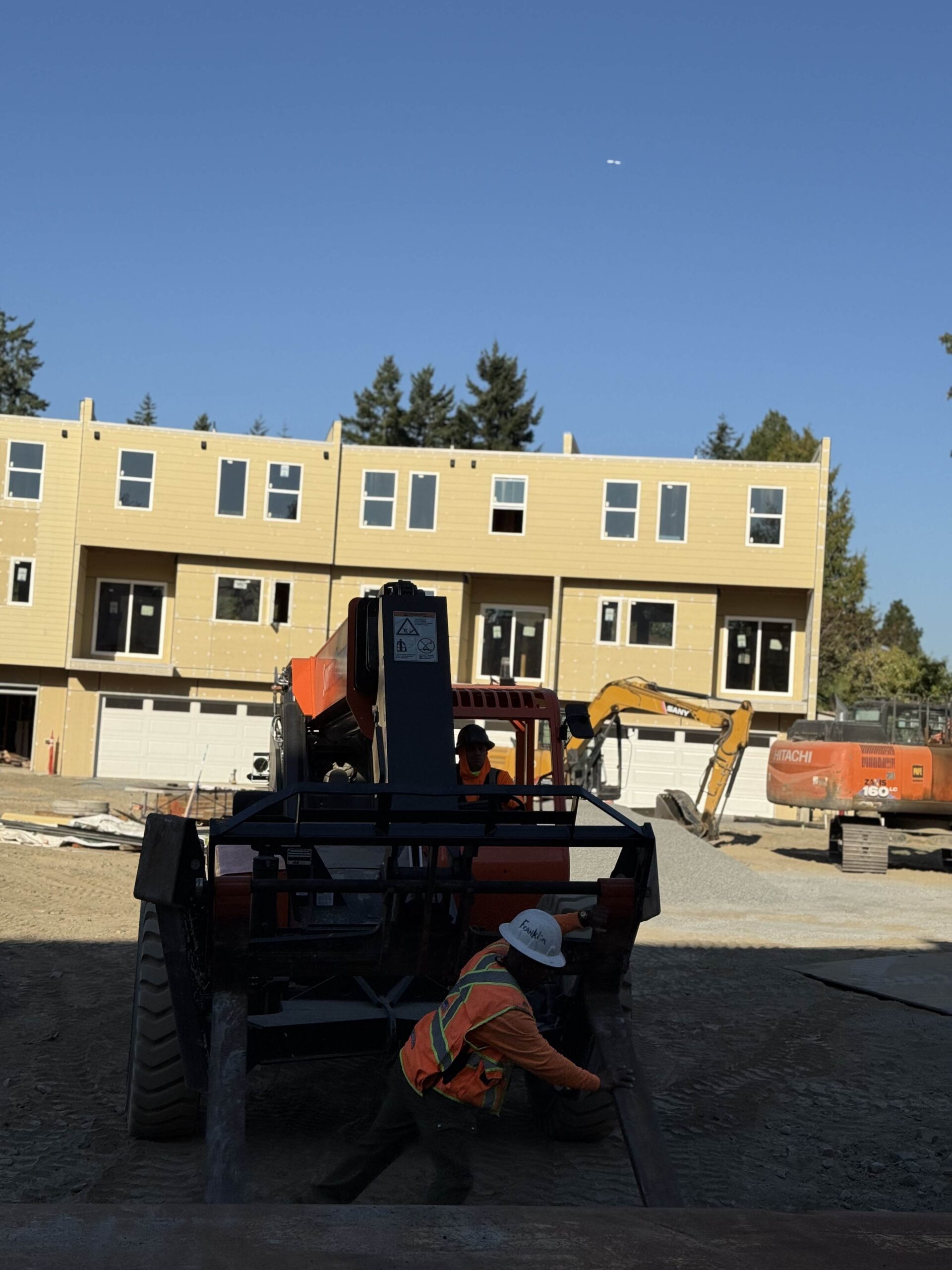 Heavy machinery, including an excavator and a forklift, on a TP Home construction site, symbolizing the large-scale equipment used for building projects.